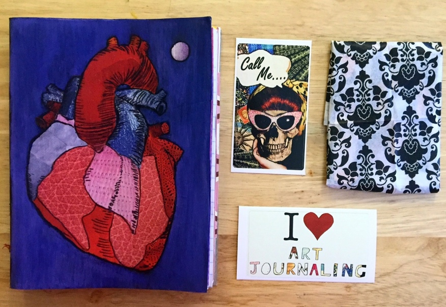 A handmade junk journal with an anatomical heart on the cover next to stickers I made, ready to send to someone